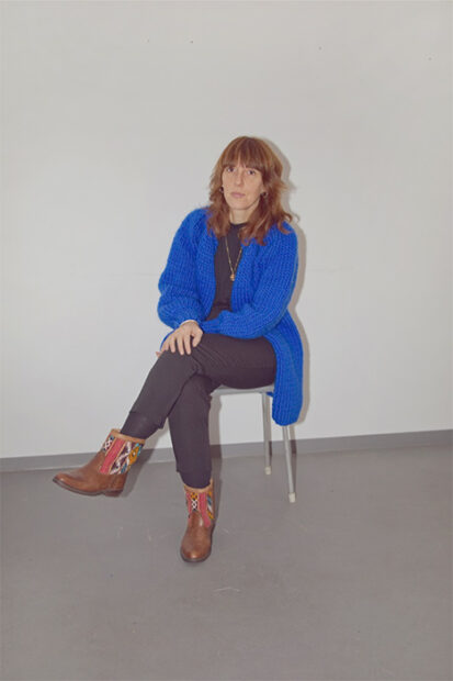 A photograph of writer Sonya Schönberger sitting in a chair in front of a white wall.