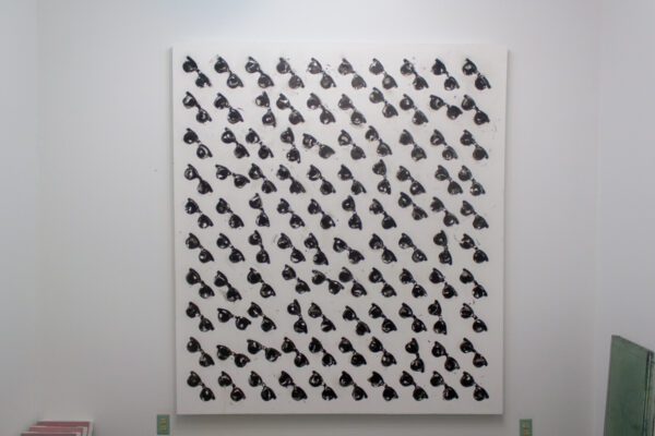 A nearly square painting of 100 black sunglasses on white hangs on a white gallery wall