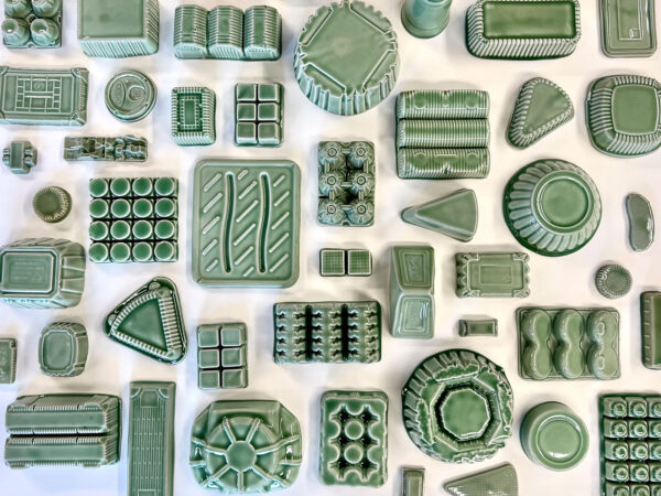 An overhead photograph of an array of green sculptures of everyday objects made by Yoonmi Nam.