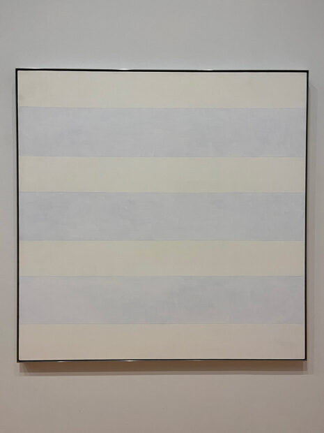A large square-shaped canvas painted by Agnes Martin. The canvas depicts 7 large rectangles whose colors alternate between white and blue.