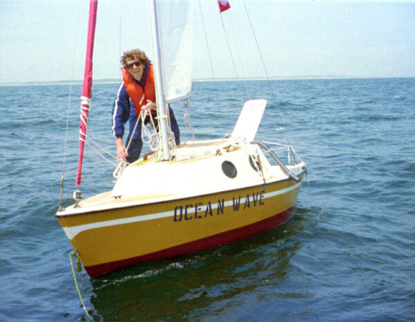 A photograph of a man standing on top of a small sailboat floating in a body of water.
