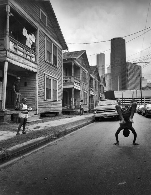 A photograph of a young Black boy doing a flip in the middle of a residential street in Houston.