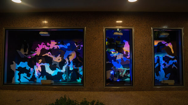 A photograph of a street-facing window installation which features colorful videos projected on abstract forms.