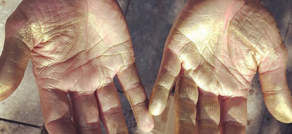 A photograph by Stephen Lapthisophon of a pair of hands covered in gold paint.