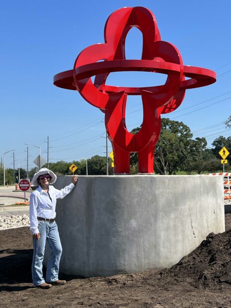 The artist standing next to the base of a large red public sculpture in a roundabout