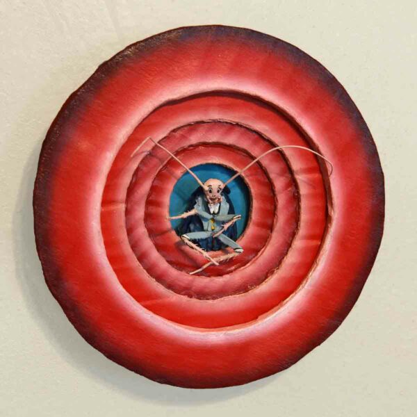 A mixed media work by Iva Kinnaird. The sculpture consists of four red concentric circles with a blue circle in the center. Layered on top of the center blue circle is a painted plastic cockroach.