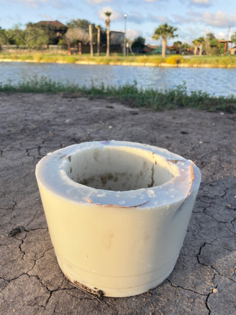 A photograph of a cylinder sitting on dry ground with a lake in the distance.
