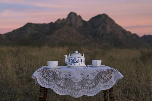 A table woith a teapot and teacups with the mountains of Las Cruces in the background