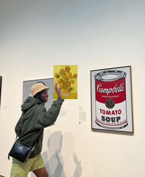 Photograph of a man, with a photoshopped Van Gogh painting in his hand. He is gesturing as if he is throwing the painting onto an Andy Warhol painting of a Campbell's soup can.