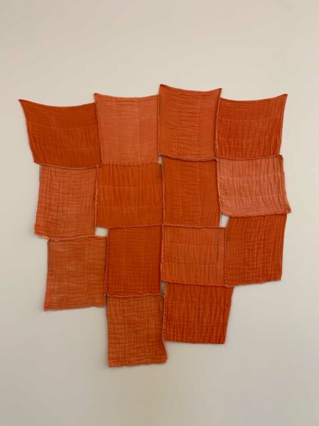 A photo of a sculpture that consists of red tea towels pinned to a wall.