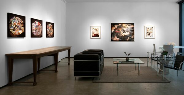 A photograph showing the interior of a white-walled art gallery. Photographs are hung on the walls of the gallery.