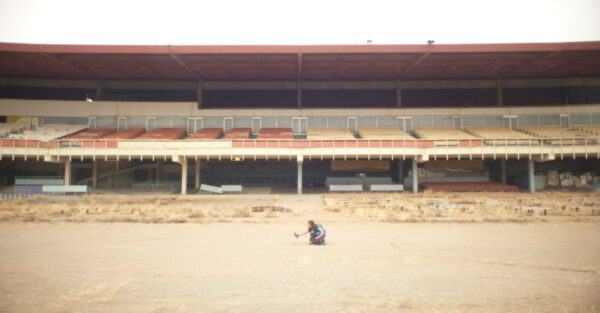En el centro de la pista de un estadio o ruedo abandonado está una figura humana agachada.
