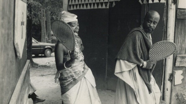 A still image from Al Santana's film "Voices of the Gods." The still image is black and white and depicts two Yoruba people who appear to be dancing and singing.