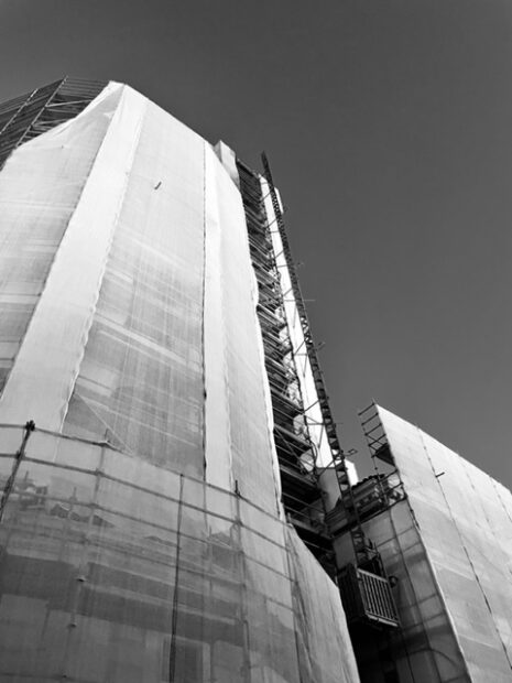 Black and white image of a building wrapped behind tarps and scaffolding.