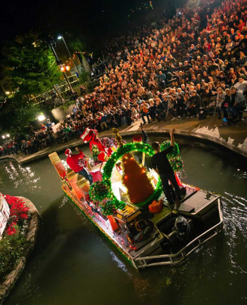 A photograph of a holiday river float moving past a large seated crowd.