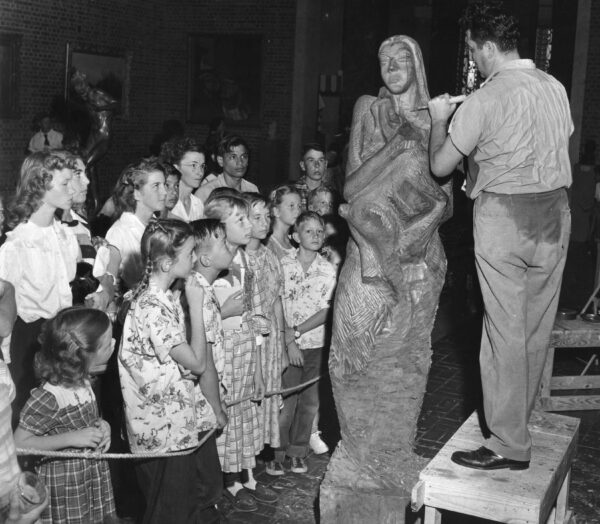 Image of the artist working on a sculpture with an audience of children