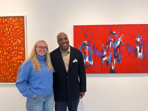 A photograph of Bailey Summers and Alfred Walker standing in a white walled gallery with two large abstract paintings behind them.