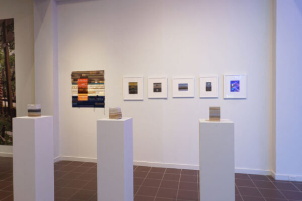 installation of various framed works hanging on the wall and three small sculptures on pedestals