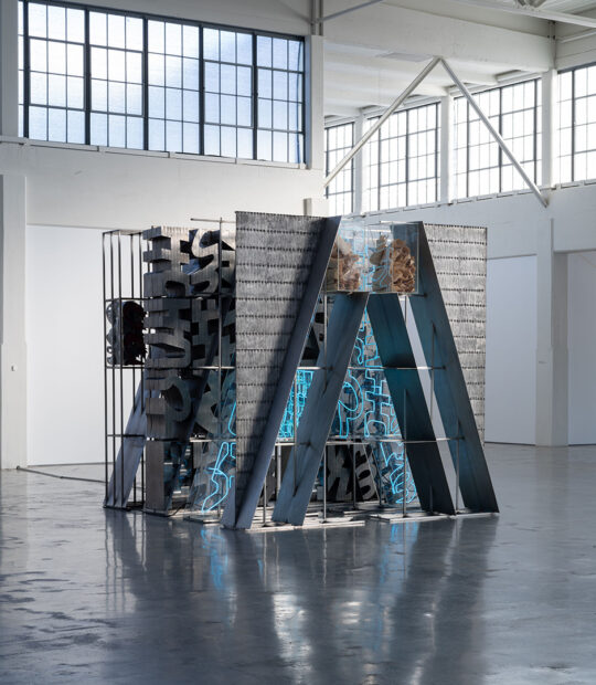 An installation image of a large-scale sculpture by Chryssa. The scupture is made from metal, neon, and plexiglass.
