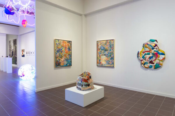 Installation view of various mixed media works on wall, and a sculpture on a plinth