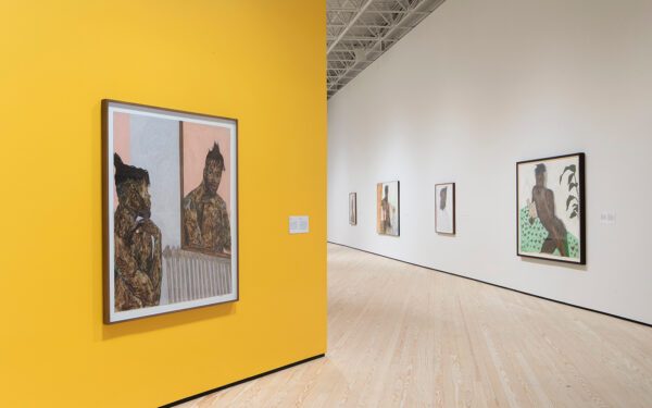 A photo of an installation of midsize figurative pantings. Some works are installed on a white wall, wile another piece is on a yellow wall.