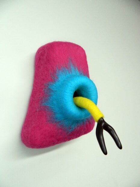 Photo of a pink felt sculpture with a two pronged black tongue coming from a blue hole
