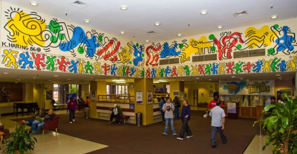A photograph of a hospital lobby. The upper walls of the lobby are decorated by brightly colored, faceless figure outlines.