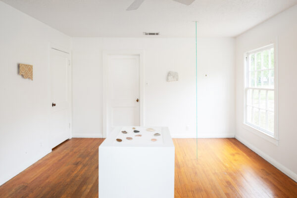 Installation view of objects on a pedestal, works on a white wall and a green sculpture bisecting the space from floor to ceiling