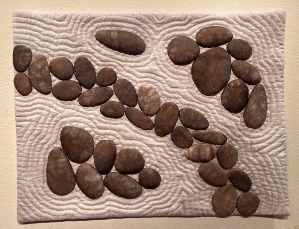 A photograph of a fabric work by Nancy K. Fisher. The piece resembles smooth stones on raked sand. 
