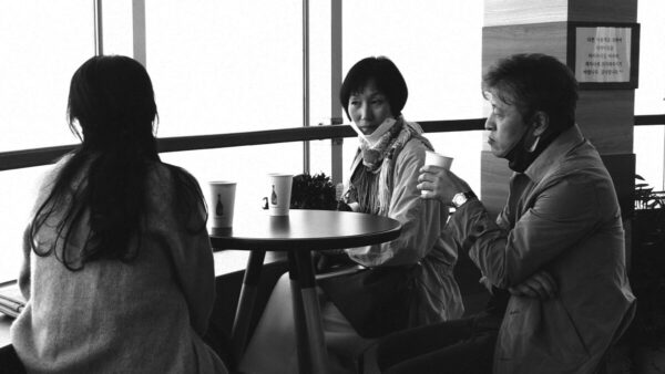 Black and white still of three people sitting at a table drinking coffee