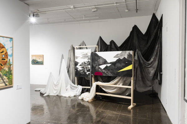 Installation view of canvas stretchers and landscape paintings with fabric hanging int he background