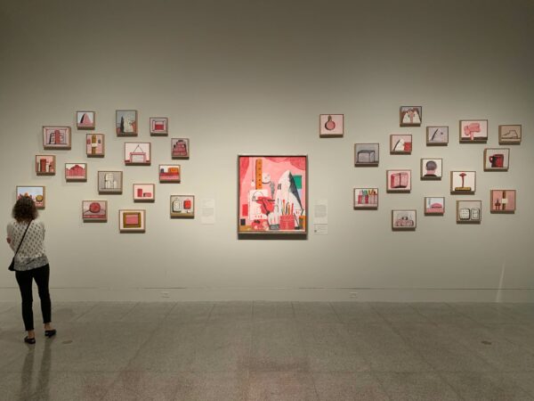 A photo featuring many small-scale paintings hung salon style on a gray wall.