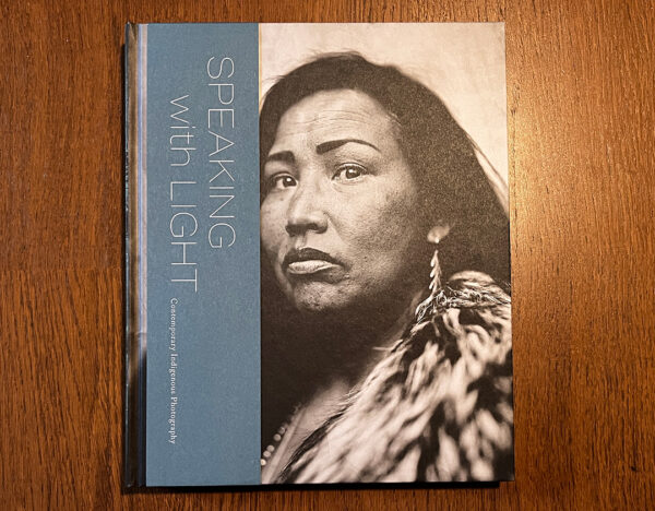 A photograph of the front cover of the book "Speaking with Light: Contemporary Indigenous Photography. The cover features a black and white photograph of an Indigenous woman.