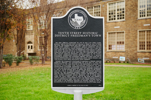 A photograph of a Texas Historical Commission Marker for the Tenth Street Historic District Freedman's Town in front of a brick building.