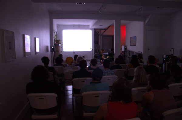 A photograph of a film screening with people seated watching.