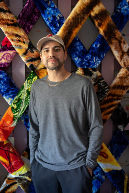 A photograph of Antonio Lechuga standing in his studio in front of a large-scale colorful installation piece.