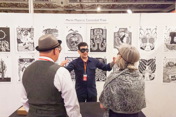 A photograph of an Martin Mazorra at a booth displaying his black and white prints.