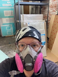 A photograph of Cary Reeder wearing a respirator mask as she cleans and packs her studio.