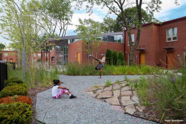 A photograph of two kids playing outside of the red brick townhomes of the Dorchester Art + Housing Collaborative in Chicago.