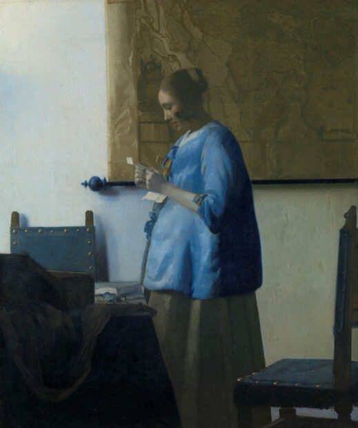 An image of a women dressed in blue. She is reading a letter, and is in profile.