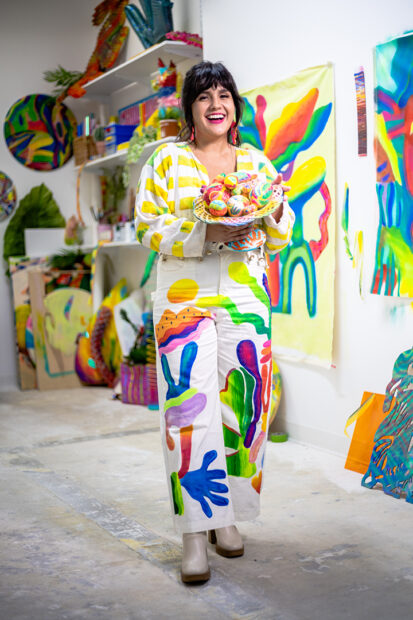 A photograph of Mariell Guzman in her studio holding a bowl of brightly painted eggs in a woven basket.