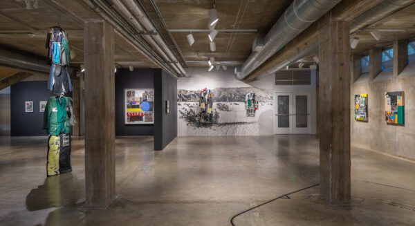 Installation view of work hanging on walls and sculptures of multicolored suits