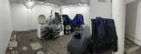 A photograph of Vincent Fink's studio covered in soot with objects stacked and covered in the center of the room.