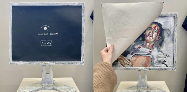 Photo of a sculpture of a computer screen with the image "sensitive content" underneath is the image of a wounded woman bleeding from her head