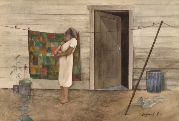 An elderly woman standing in front of a quilt