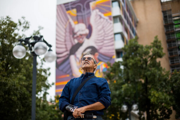 A photograph of artist Jesse Treviño stands in front of his nine-story mural titled "The Spirit of Healing."