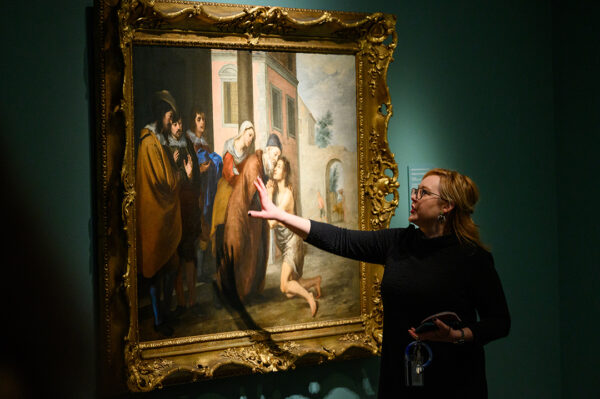 A photograph of Amanda Dotseth gesturing toward a painting while talking about the work.