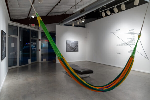 Installation view of art in a gallery. A hammock hangs in the foreground.