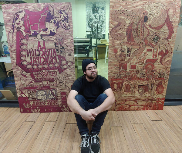 A photograph of Ben Muñoz sitting in front of two large wood carvings.