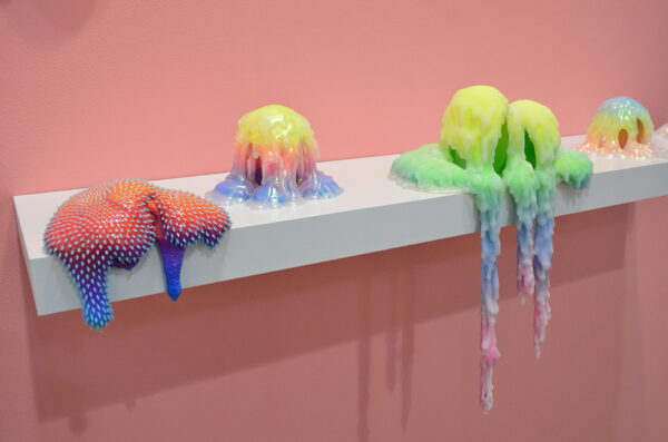 Brightly colored, drippy-looking sculptures hang over the edge of a pedistal.
